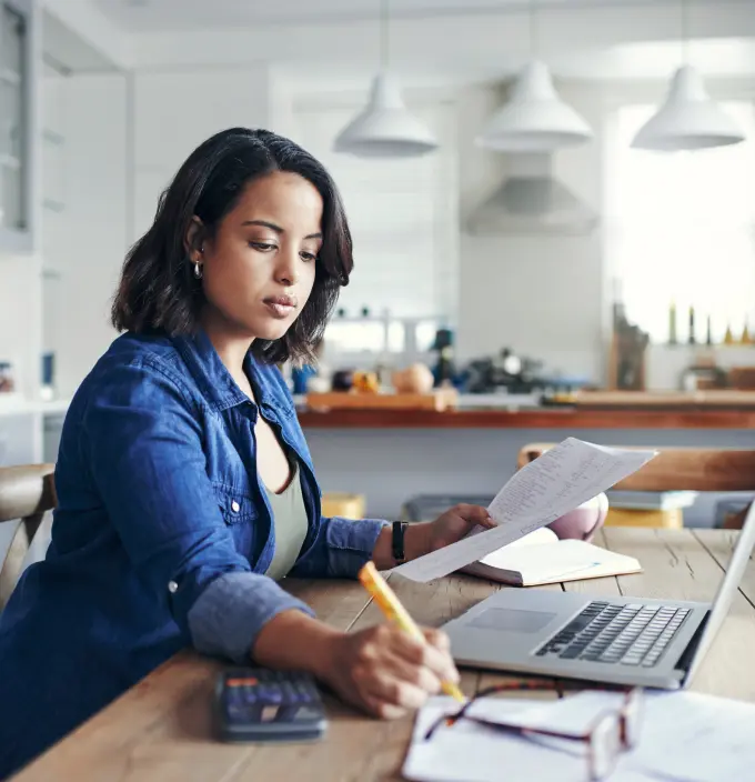 Woman working on her laptop while reviewing paperwork.