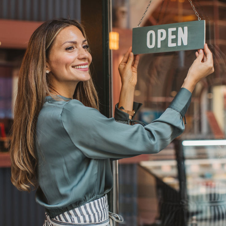 Woman turning sign in shop window to "open"