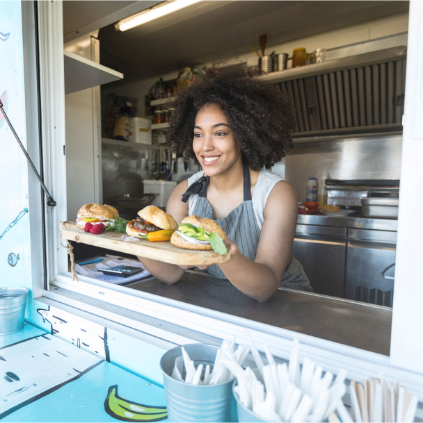 Woman serving hamburgers through a food cart window.