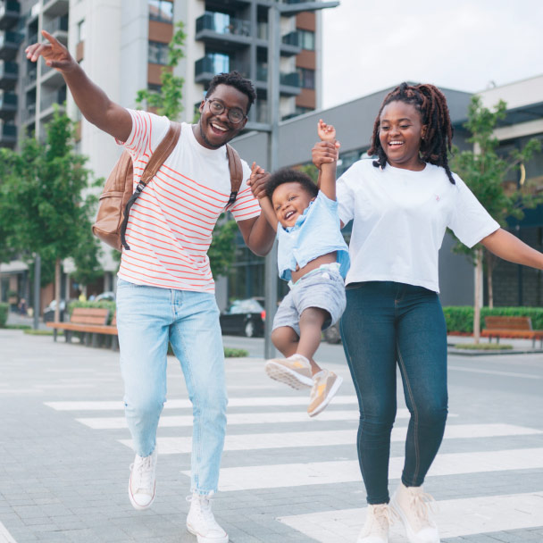 A happy couple swings their child as they cross the street.