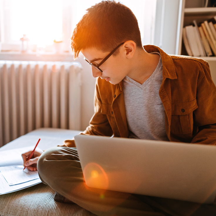 Teen studying in his room with laptop and notebook.