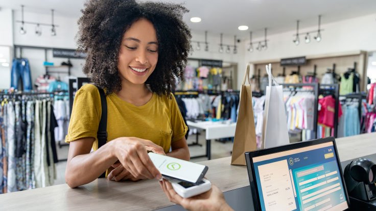 A woman uses her mobile phone to pay for a purchase at a clothing store.