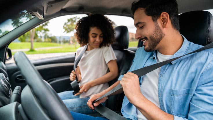 Couple in a car putting on their seat belts.