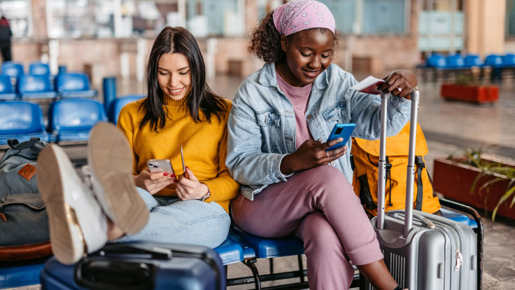 To women sit in the airport waiting for their flight.