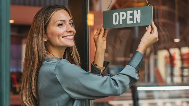 Woman turning her shop sign to "Open."